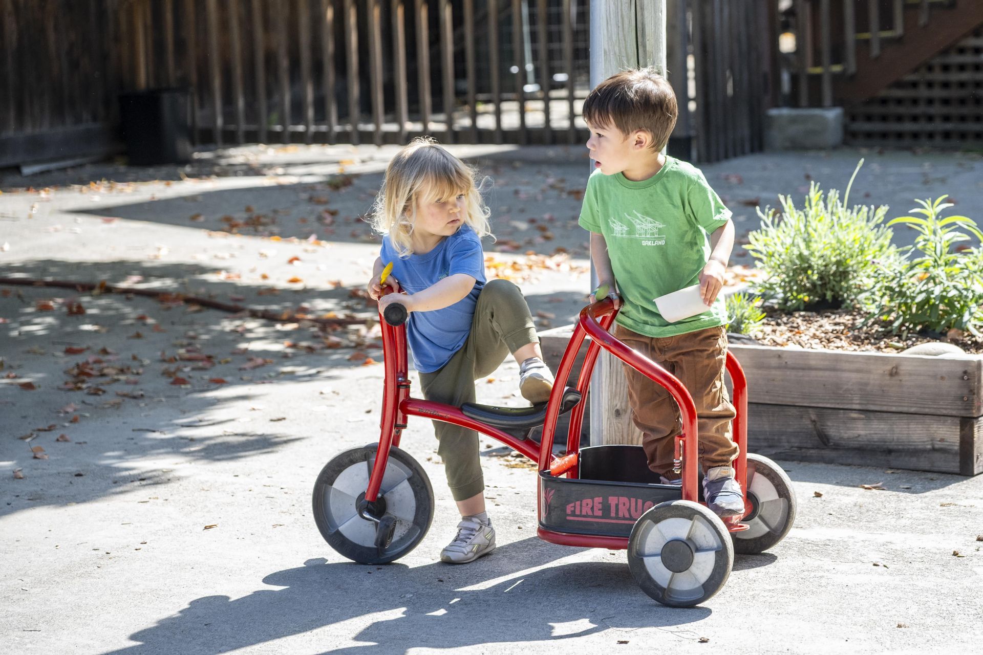 Montessori children are riding a tricycle in a playground.