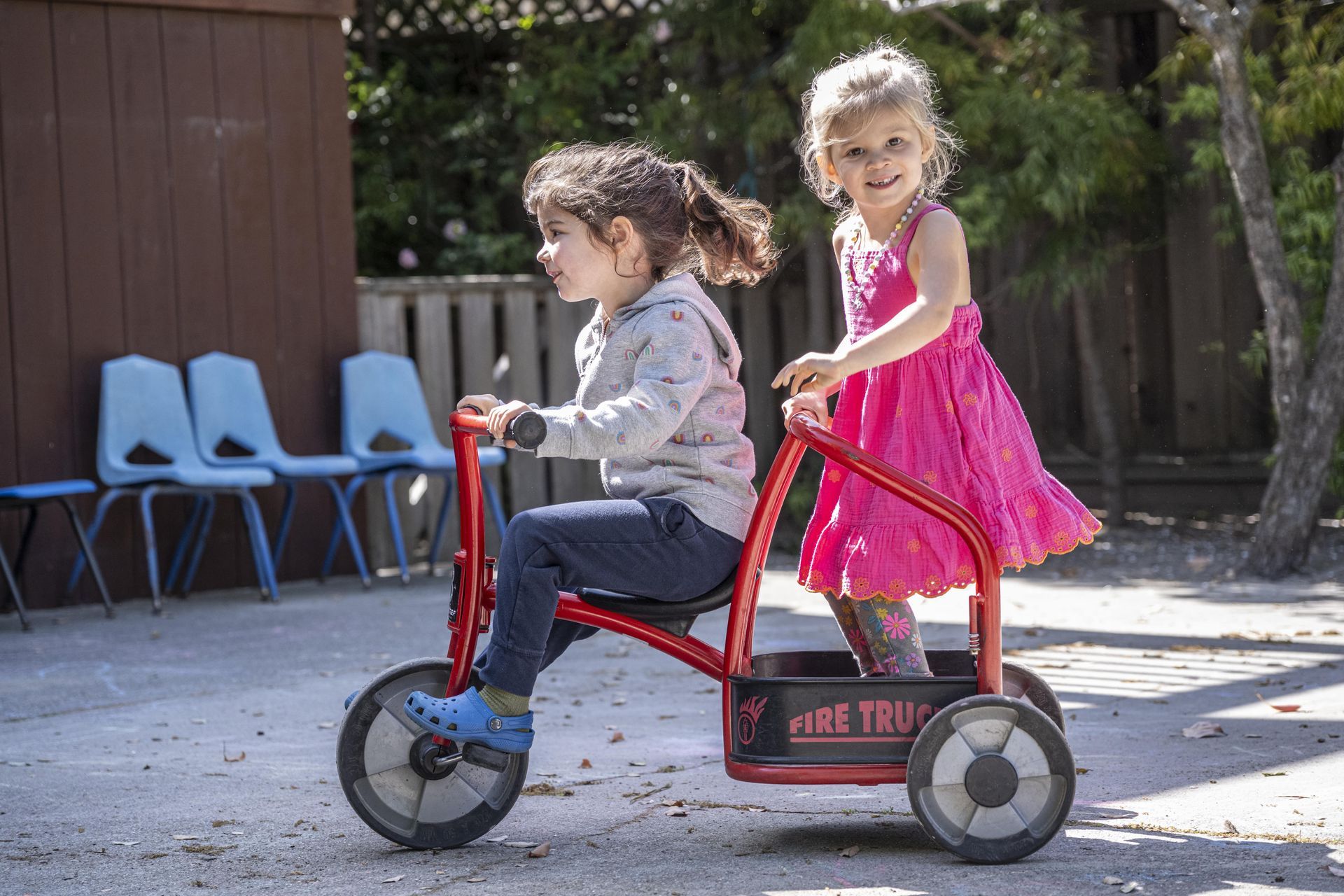 Montessori children are riding a tricycle in a playground.