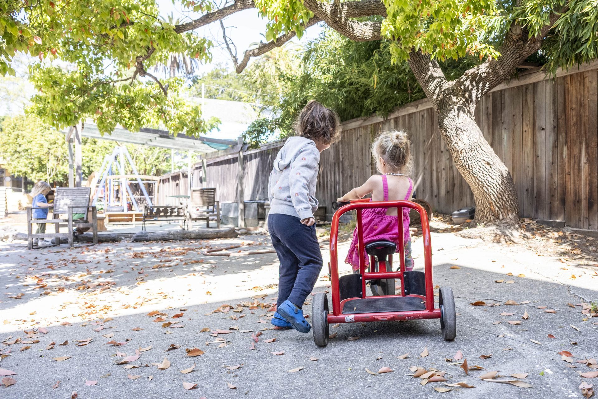 Montessori children are playing with a red cart.