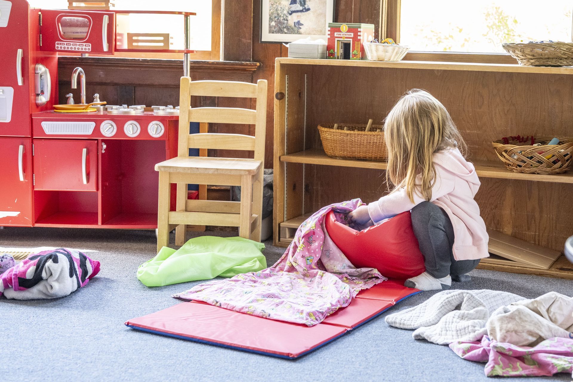 A Montessori child is sitting on a red bean bag chair in a room.