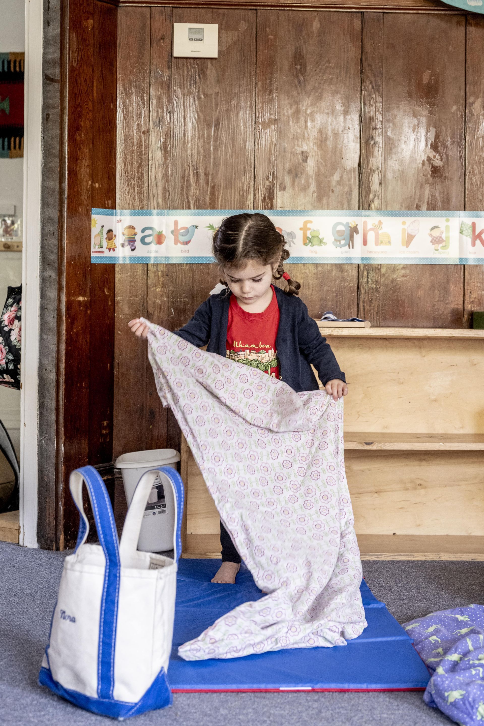 A Montessori child is holding a blanket in a room.