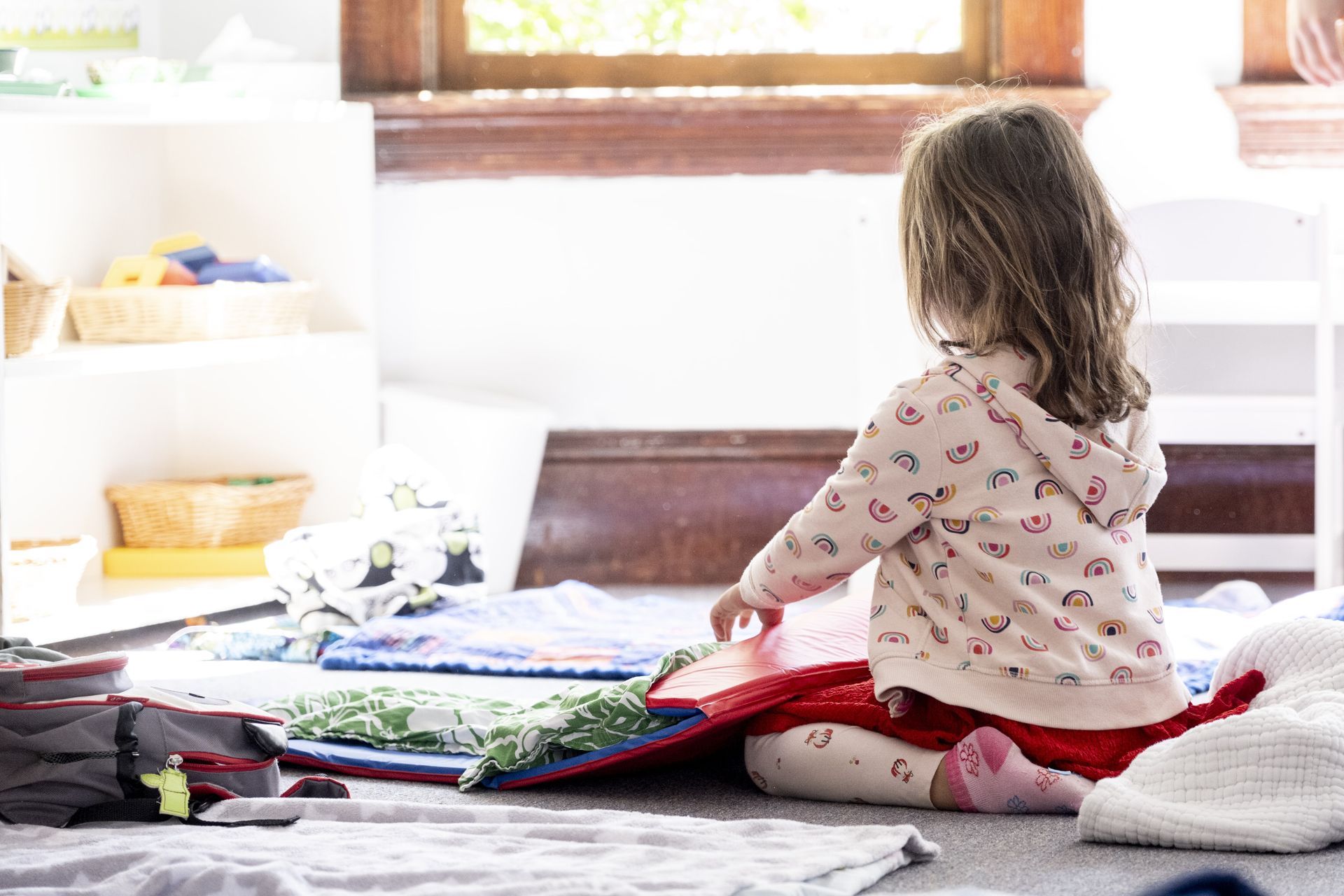 A Montessori child is sitting on the floor looking out a window.