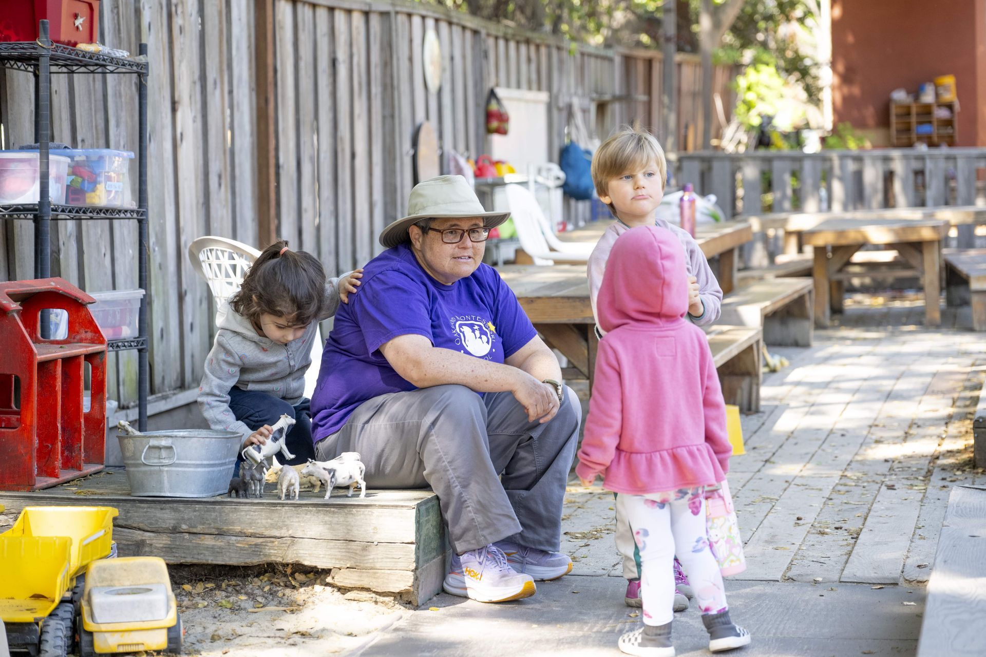 A Montessori guide is sitting on a bench with children.