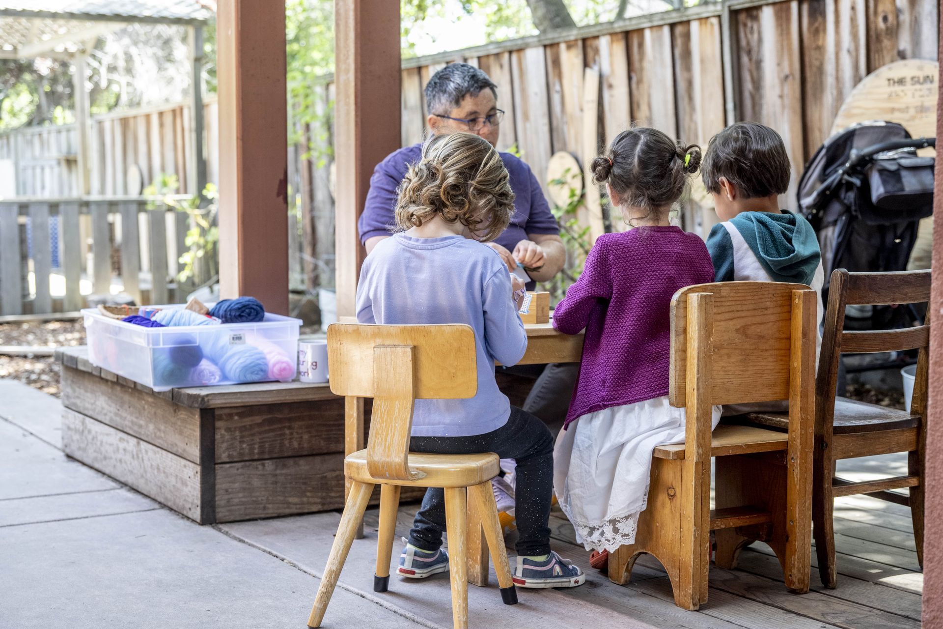 Montessori children are sitting at a table outside with a guide