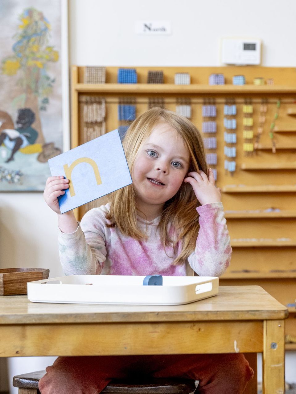 A Montessori child is sitting at a table holding a piece of paper.