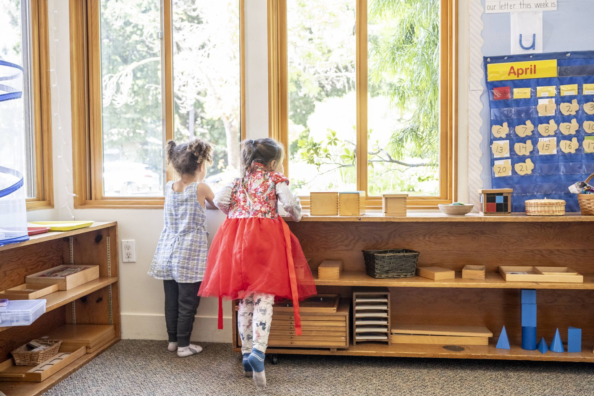 Montessori children are looking out of a window in a classroom.