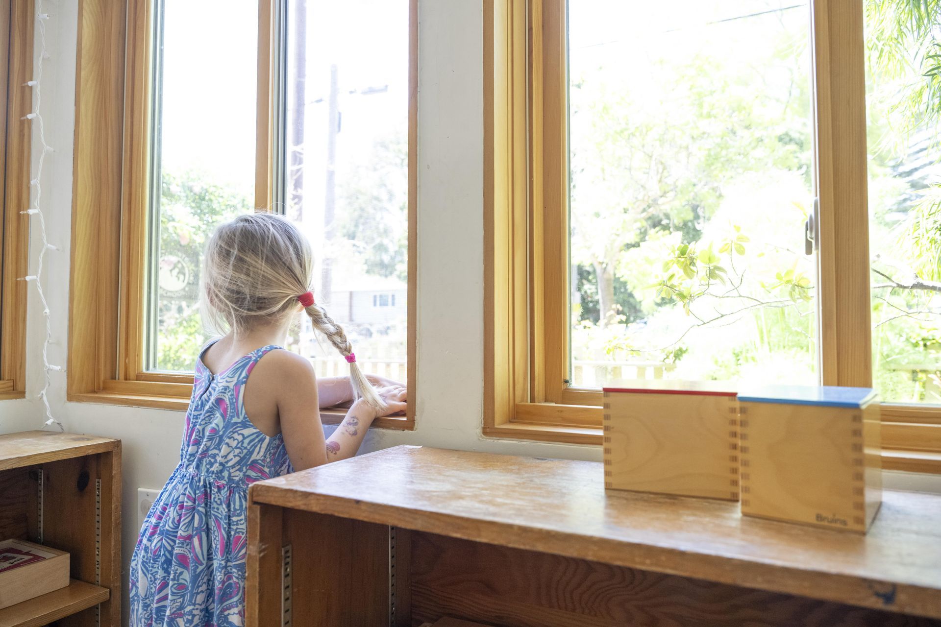 A Montessori child is standing in front of a window looking out.