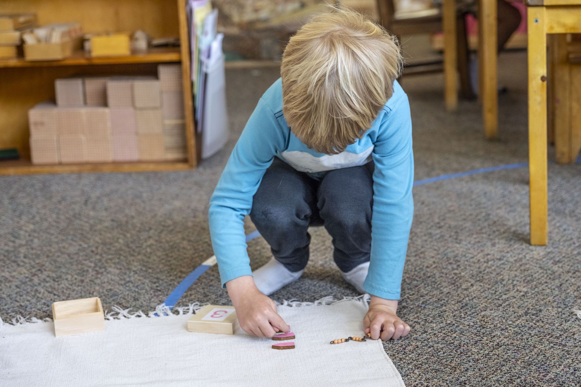 Montessori child is kneeling on the floor working with math materials.