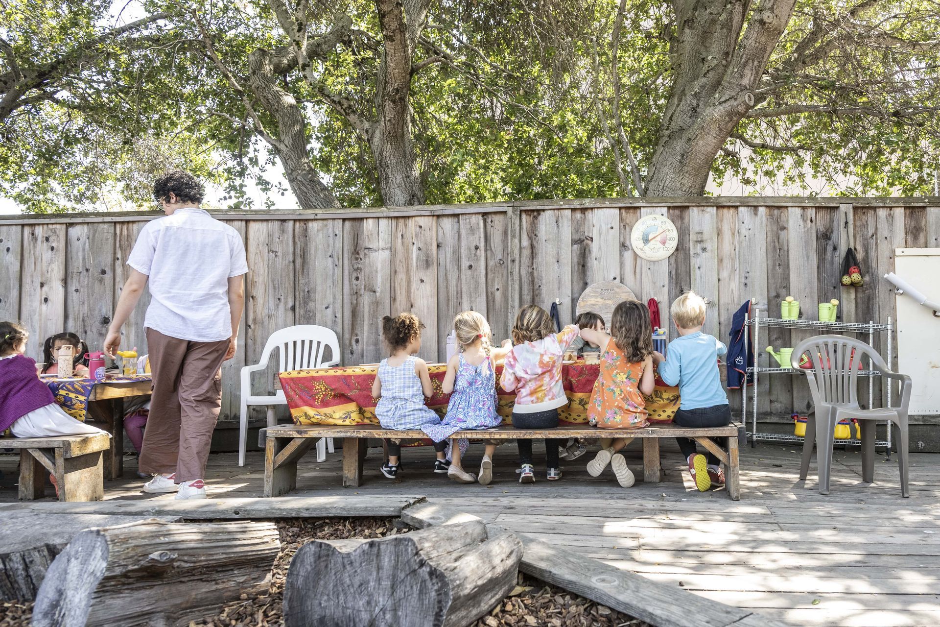 A group of Montessori children are sitting at a picnic table outside.