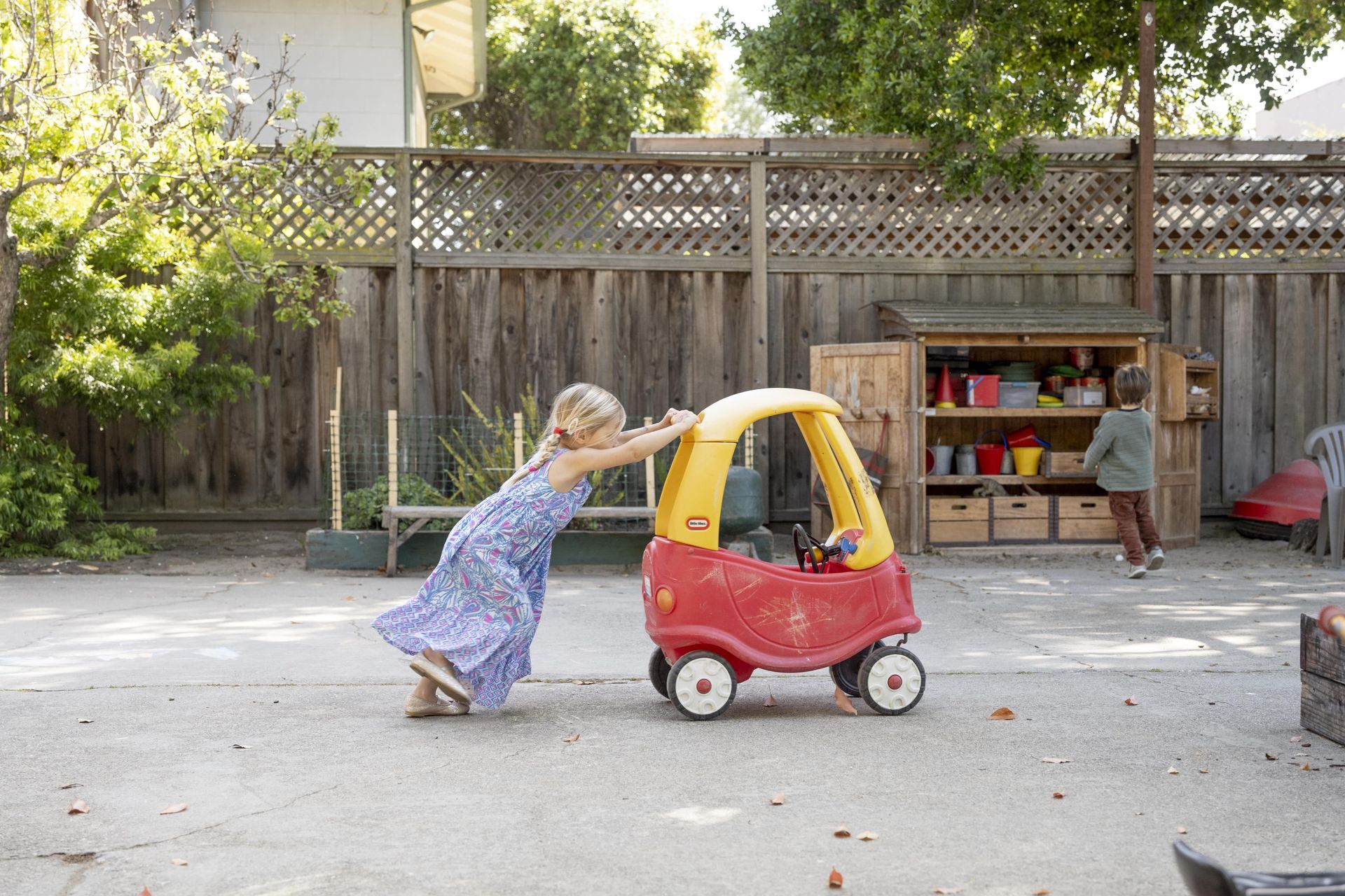 A Montessori child is pushing a toy car in a yard.