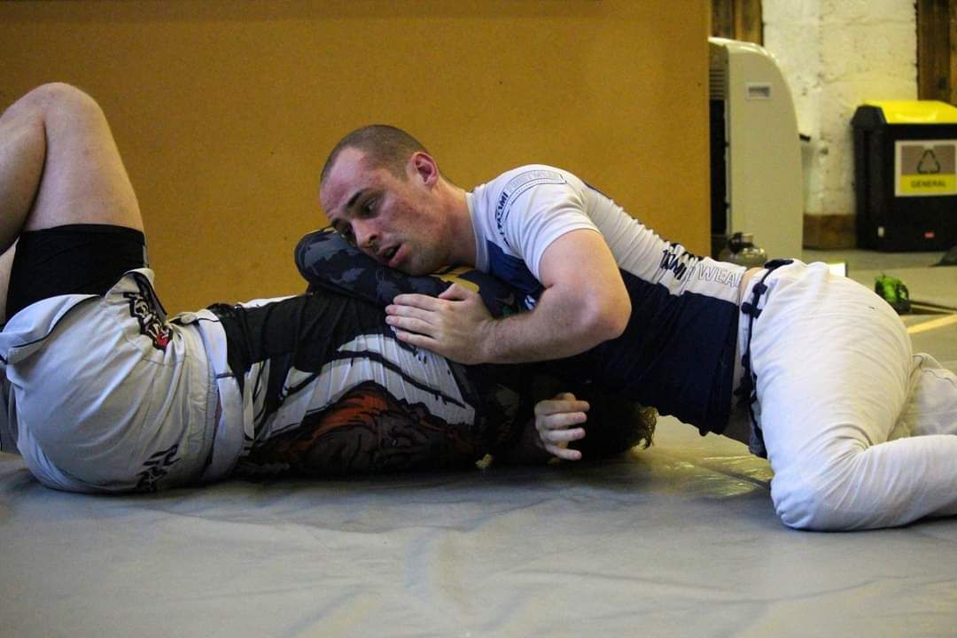 Two people grappling on a mat in a martial arts training room