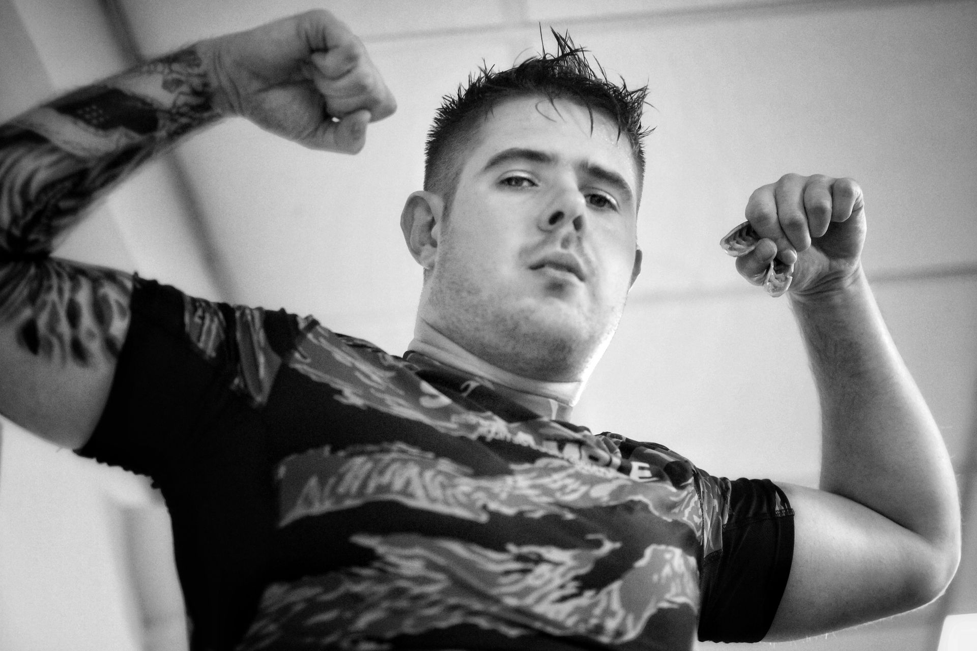 Man flexing both arms in a black-and-white photo, wearing a camouflage shirt