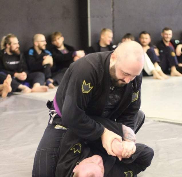 Martial arts class with two men grappling on mats while others watch in the background