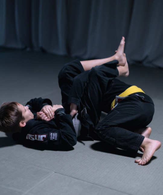 Two people practicing grappling on a mat, one pinning the other in a gym setting.