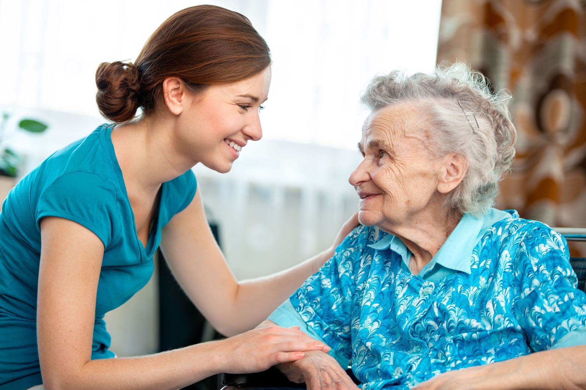 A caregiver in a blue shirt smiles warmly while resting a hand on the arm of a person in a blue patterned top.