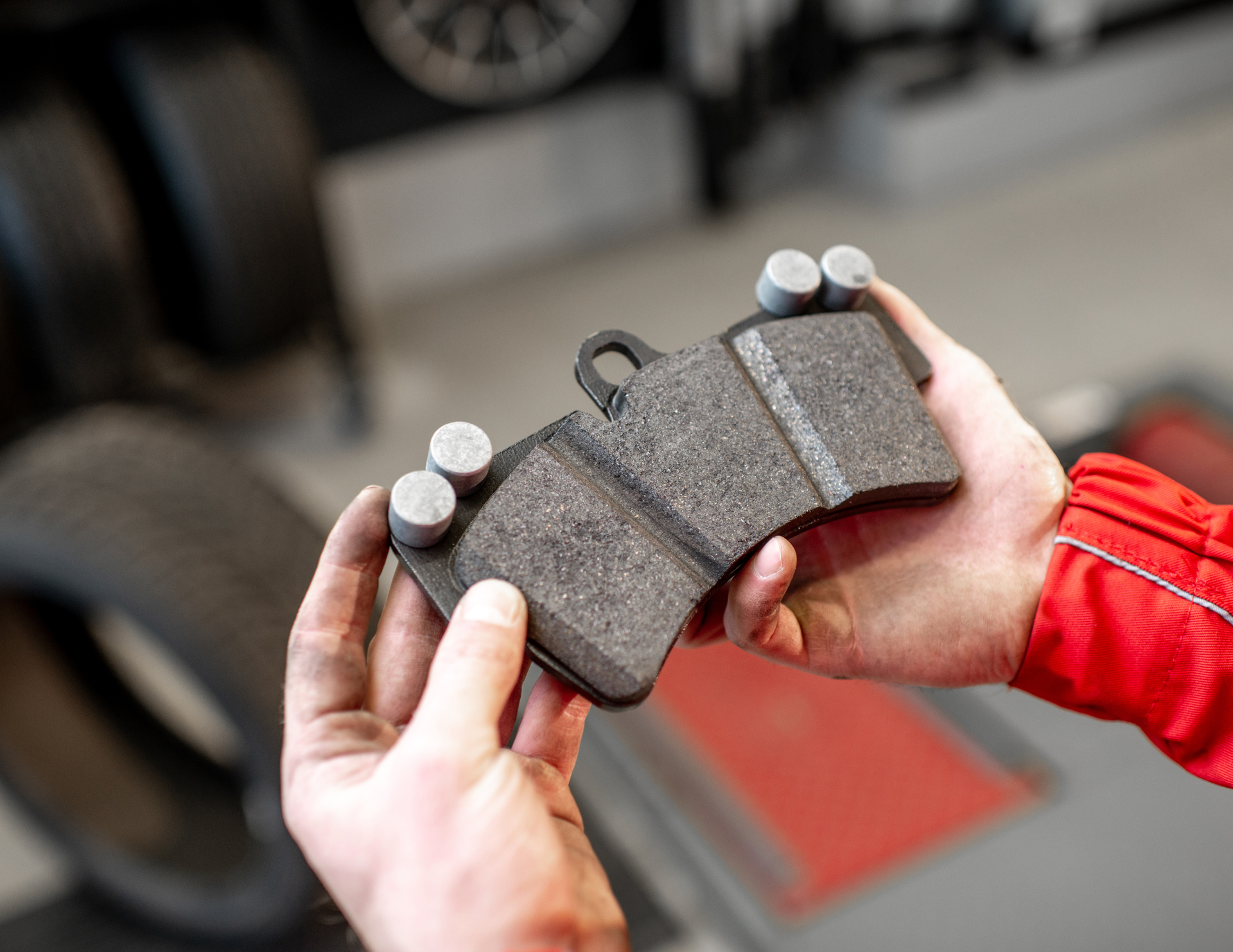 Person holding a new brake pad; blurred car parts in the background.
