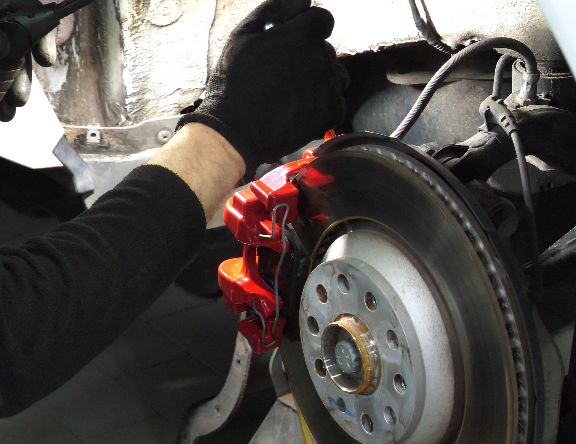 A person in black gloves working on a red brake caliper and rotor of a vehicle.
