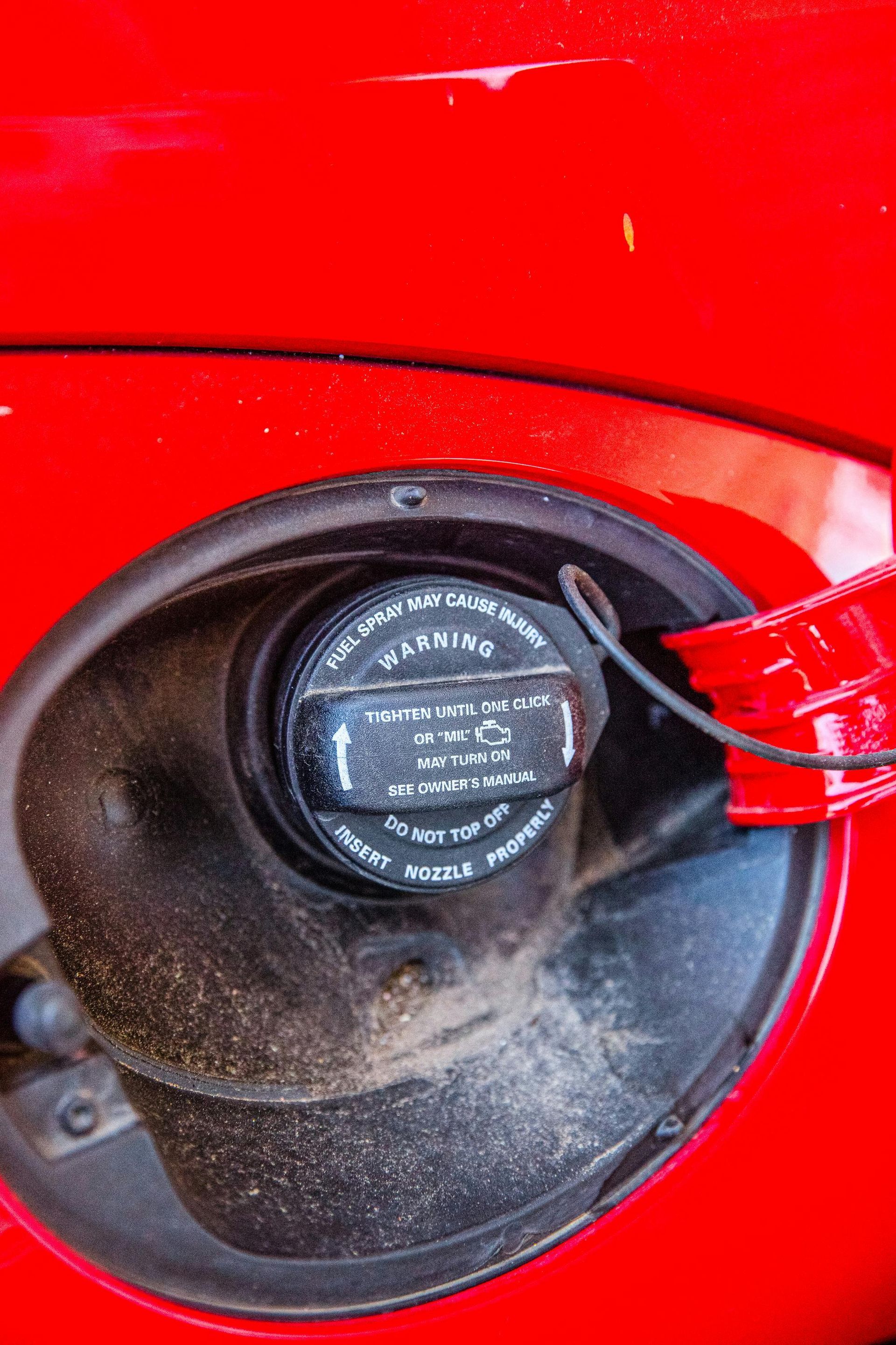 Black gas cap in red car's fuel door, with safety warning text.