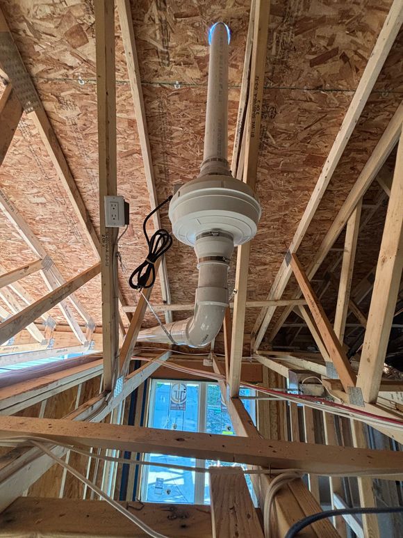 An attic with exposed wooden beams, a ventilation system, and a pipe leading to the outside.
