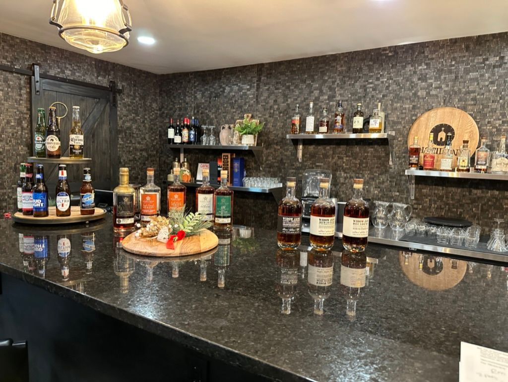 Home bar with a black granite counter, liquor bottles, and a tray of snacks against a patterned wall.