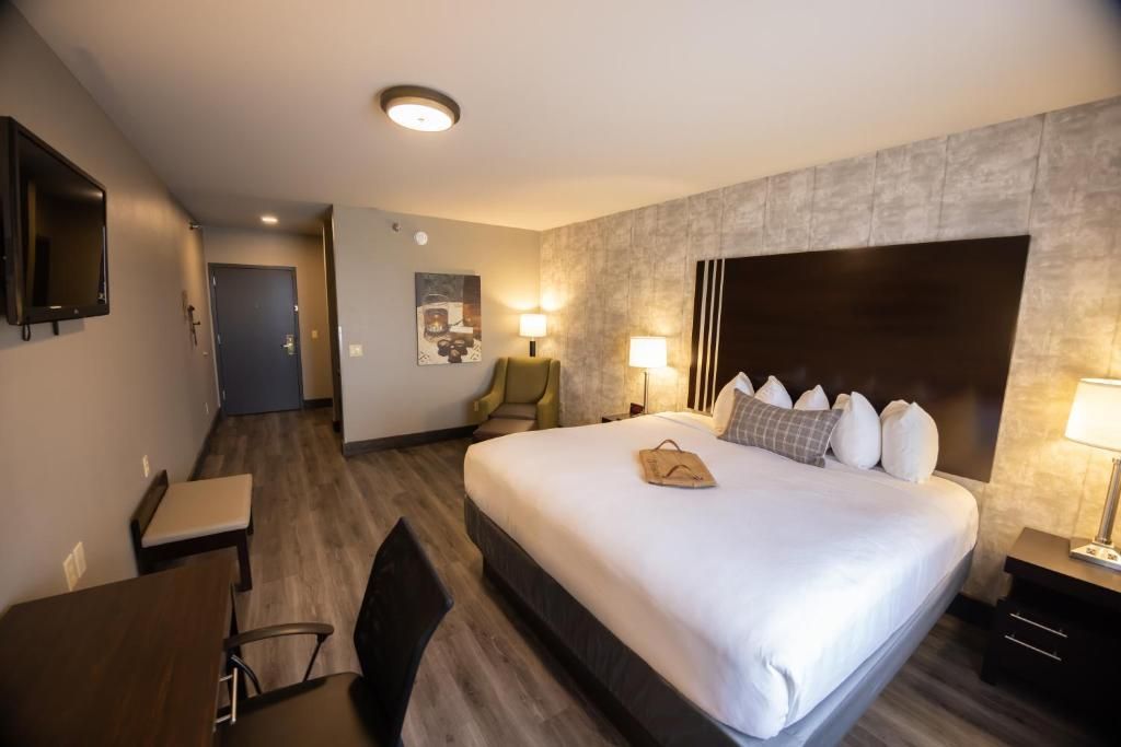 Hotel room with king bed, desk, lamps, and hallway view in warm lighting