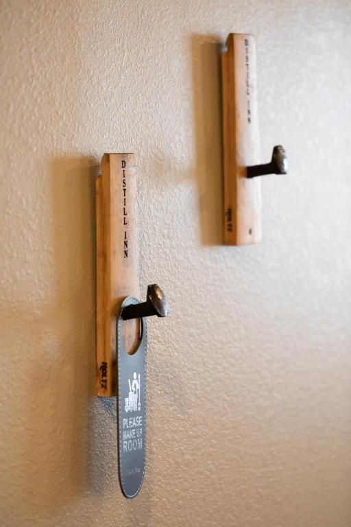 Two wall-mounted wooden handles with metal hooks, one holding a gray tool on a beige wall.
