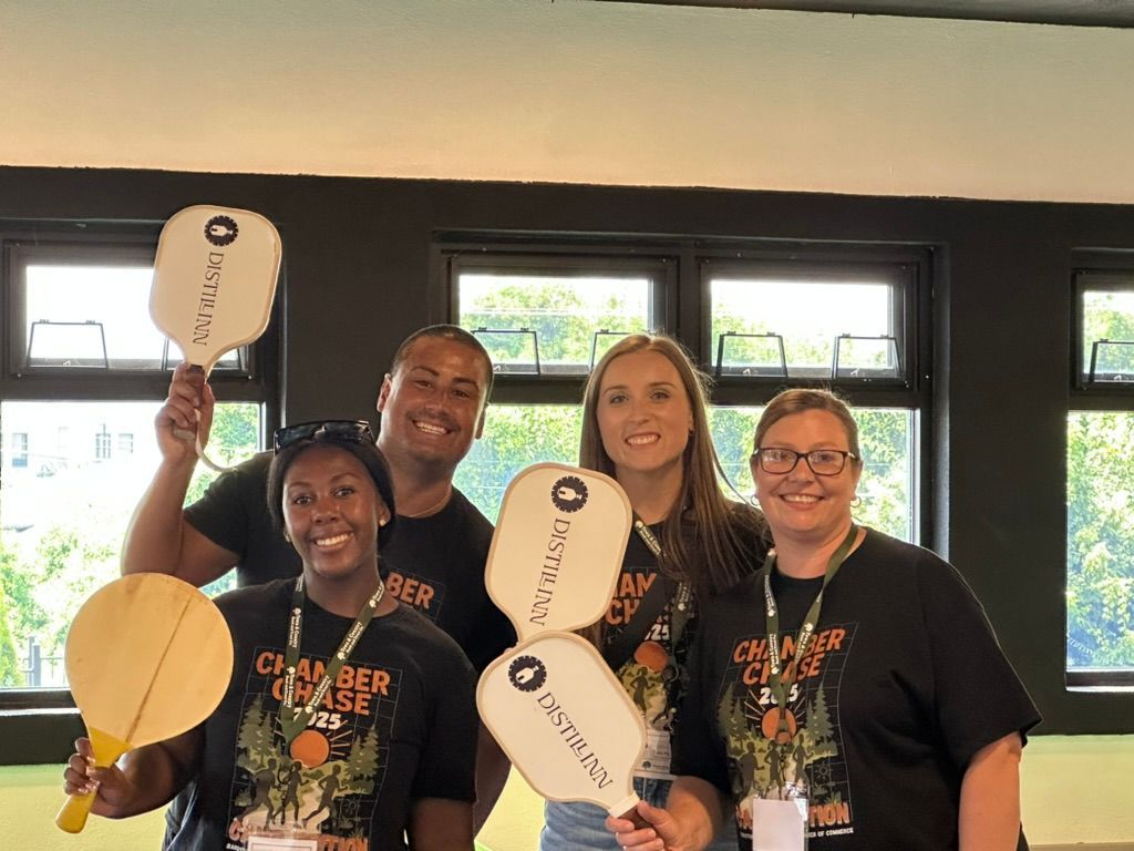 Four people posing indoors, smiling and holding paddles and a round wooden plaque.