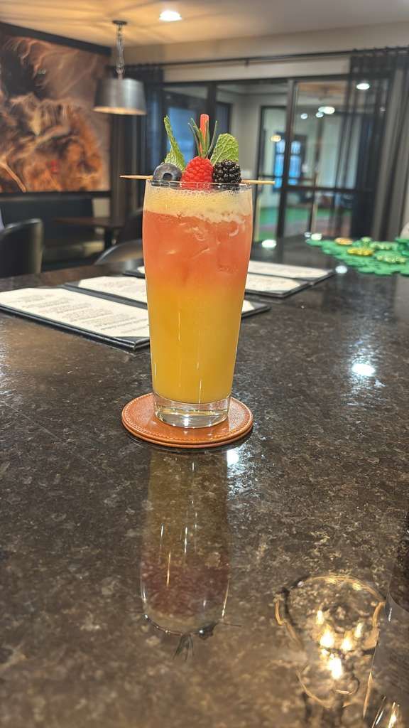 Tall orange drink with berries and a citrus slice in a glass on a bar counter