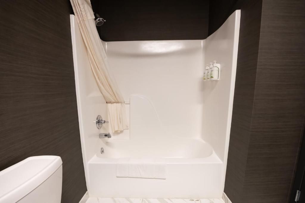 White bathtub shower alcove with cream curtain in a dark wood bathroom, with a wall-mounted showerhead and shelf