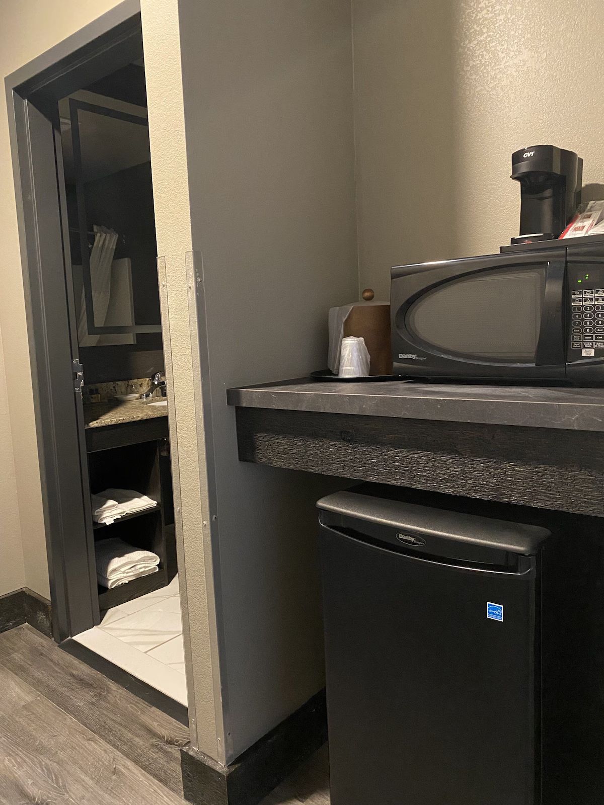 Small kitchenette with a mini fridge, microwave, counter, and open pantry shelves.