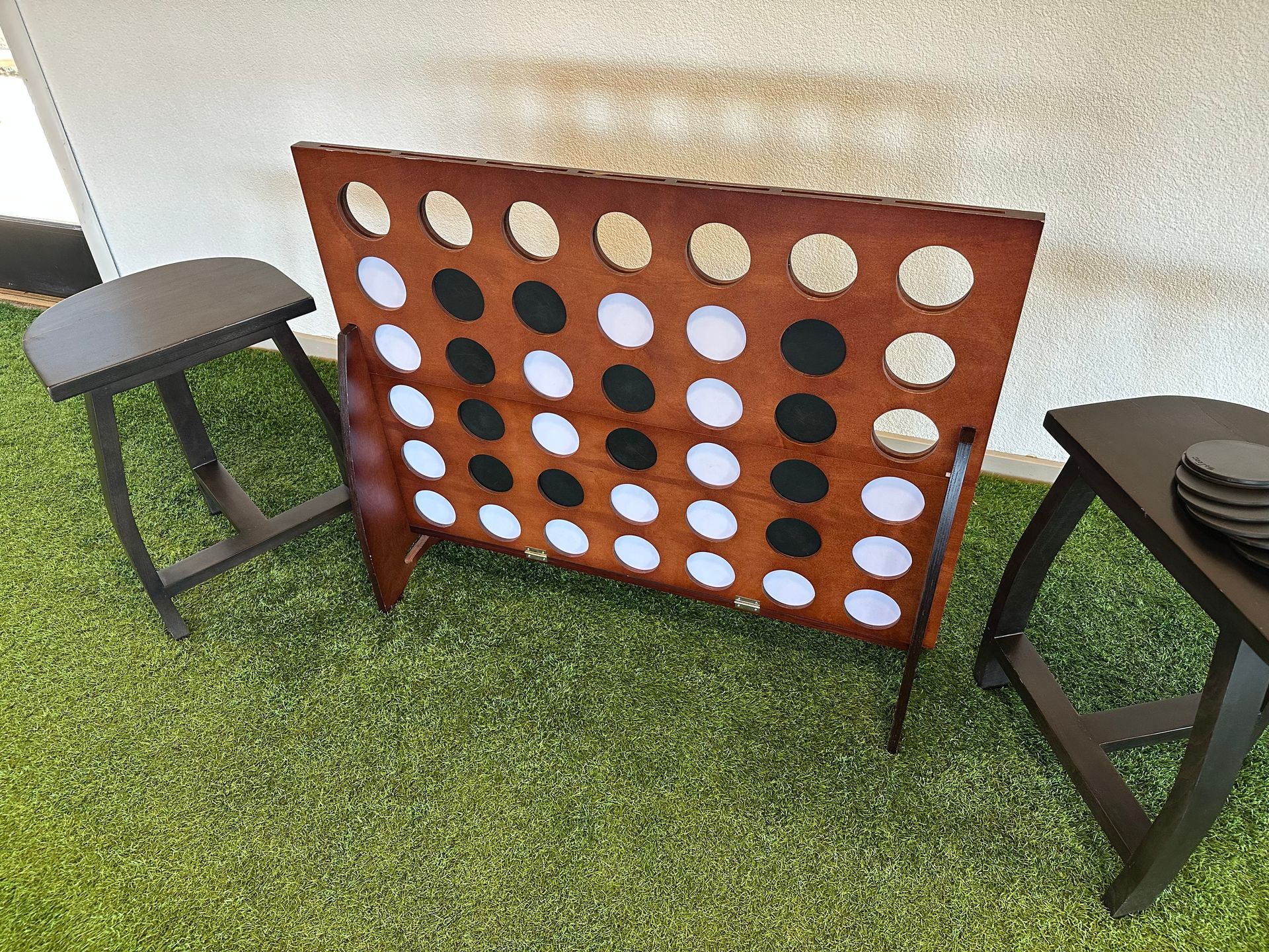 Large outdoor connect-four game on green turf between two small black stools.