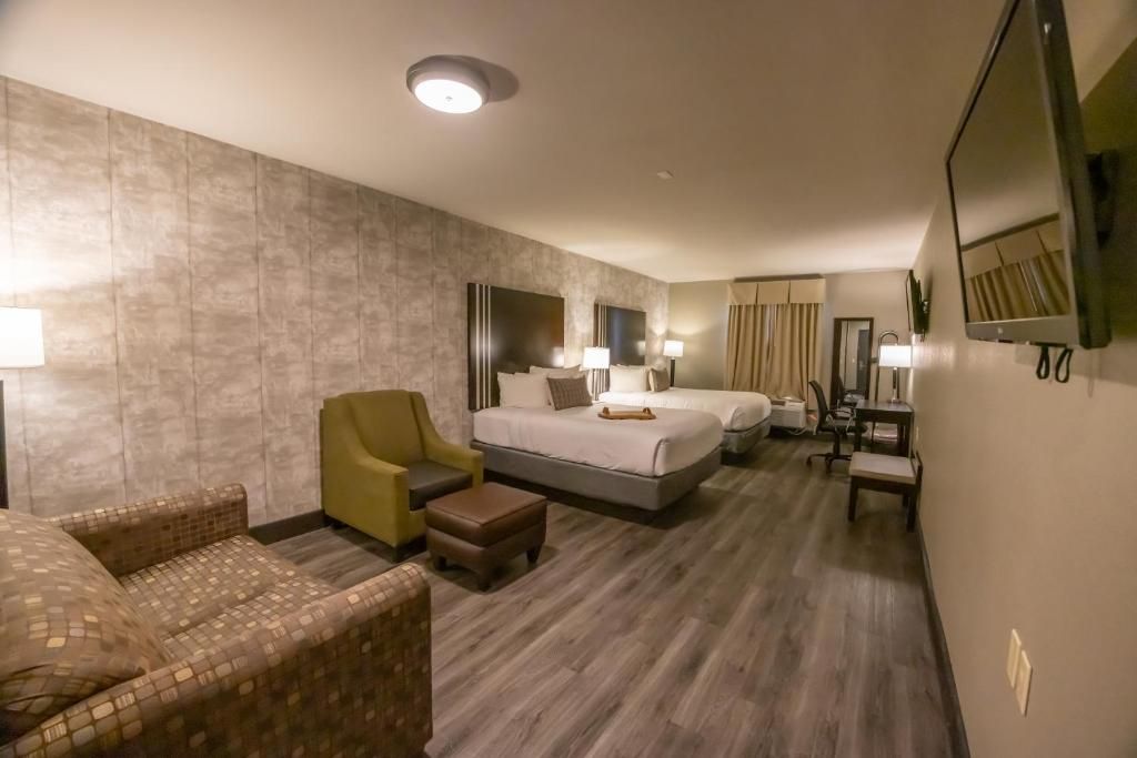 Modern hotel room with two beds, green chair, wall-mounted TV, and large window curtains