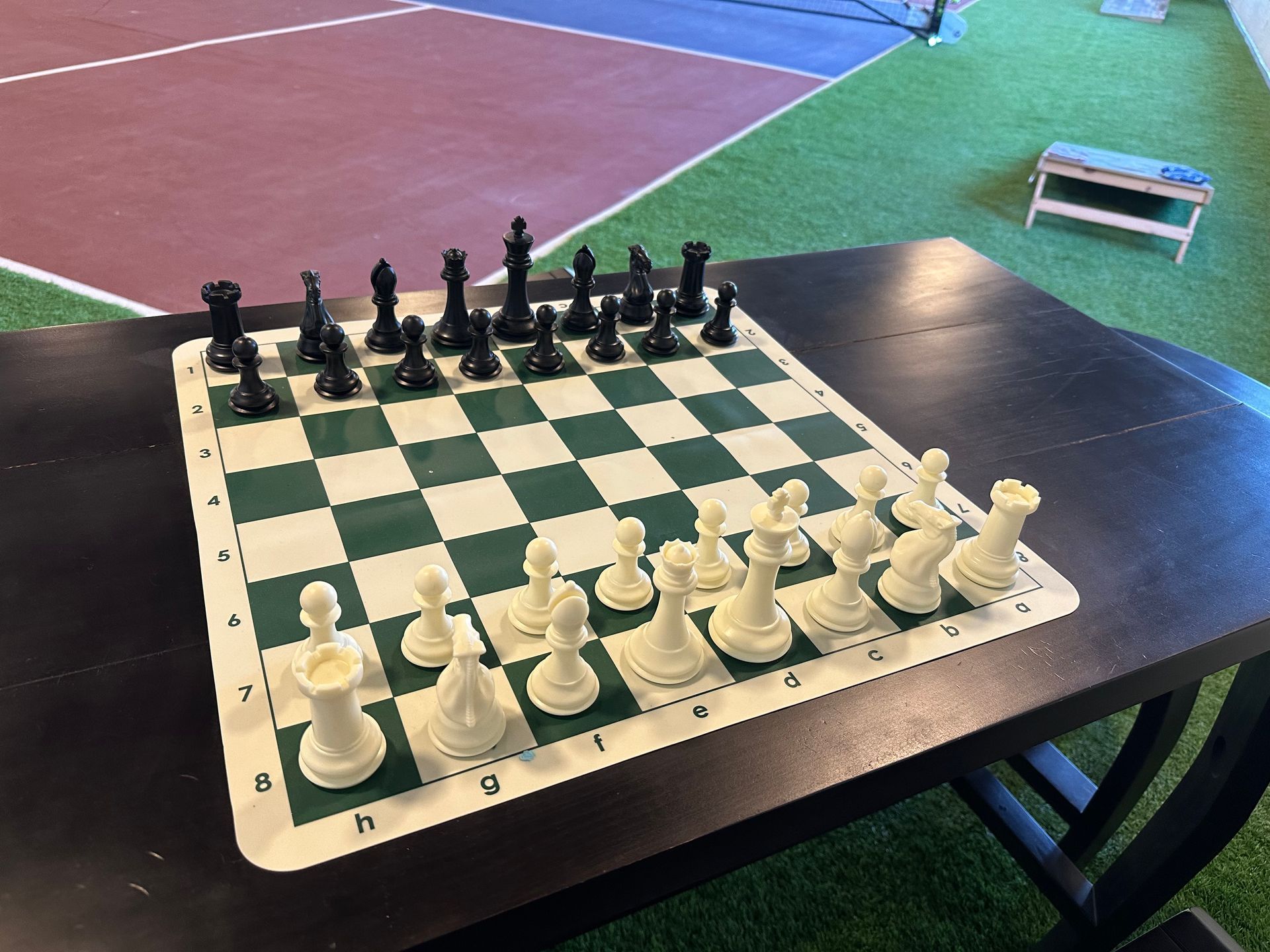 Chessboard with black and white pieces set up on an outdoor table near a court