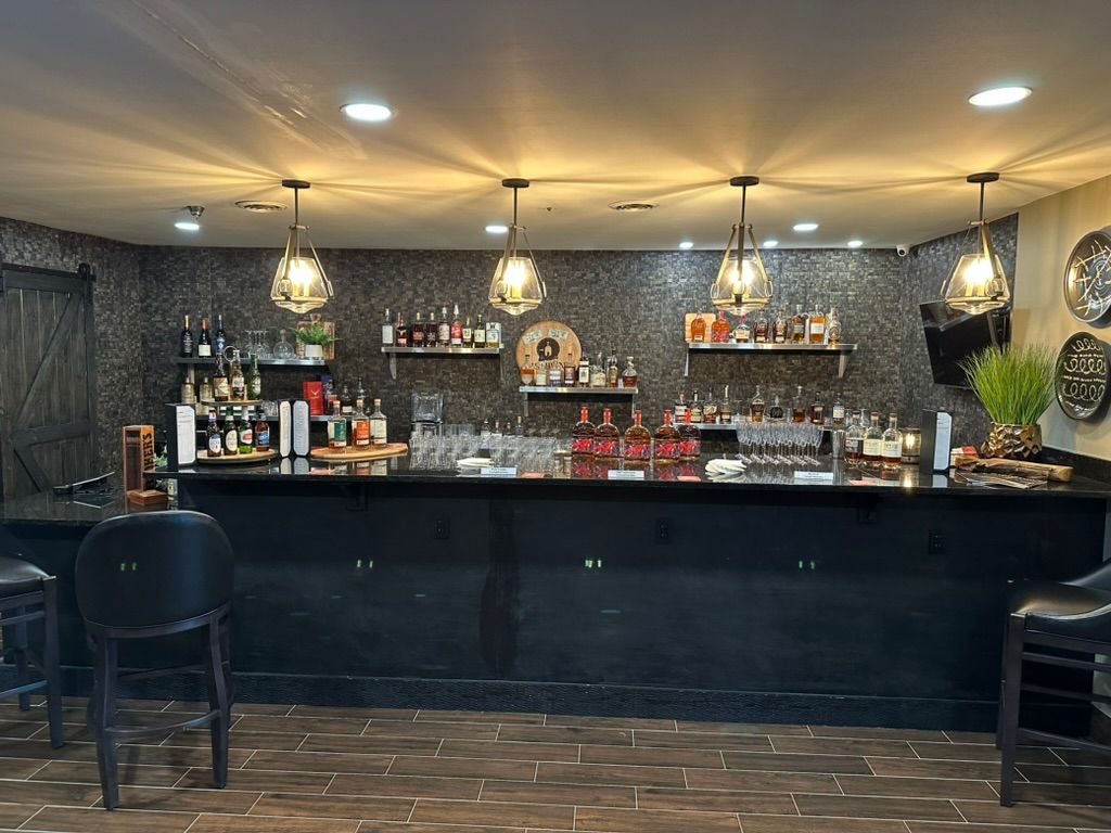 Stylish bar interior with black counter, hanging lights, liquor shelves, and two chairs in front.