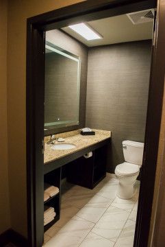 Small restroom with a toilet, vanity sink, mirror, and beige tiled walls and floor.