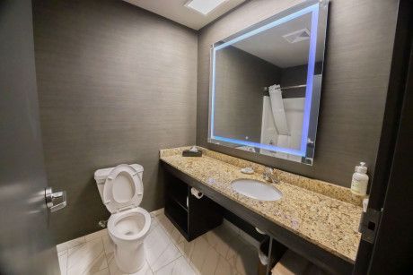 Modern restroom with granite vanity, mirror, sink, and open toilet lid under warm lighting