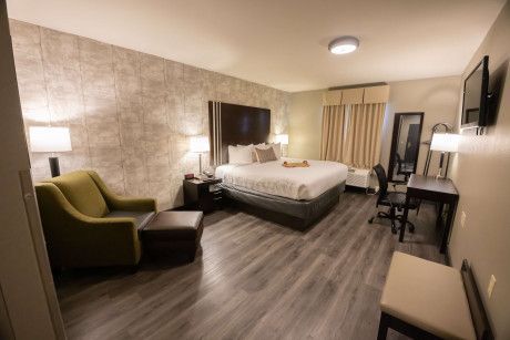 Modern hotel room with a bed, armchair, desk, and large mirror on wood flooring