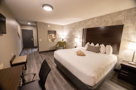 Modern hotel room with a king bed, bedside lamps, desk, and gray carpet