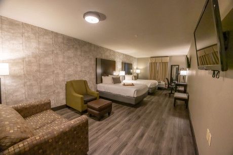 Modern hotel room with two beds, a chair, wall-mounted TV, and wood-look flooring