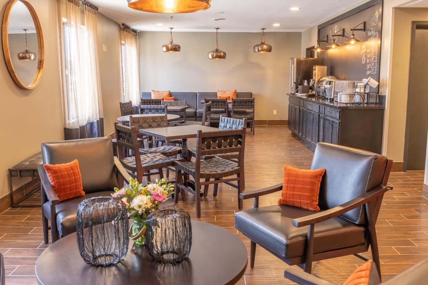 Cozy hotel lounge with leather chairs, tables, warm lighting, and a buffet area in the background