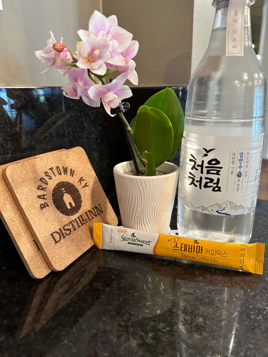 Assorted Korean craft items: pink flowers in a pot, bottles, and packaged goods on a dark countertop.