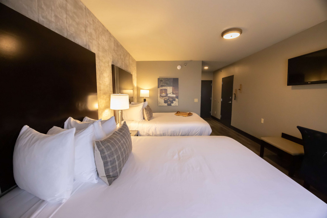 Hotel room with two white beds, bedside lamps, wall art, and a TV on the right wall.