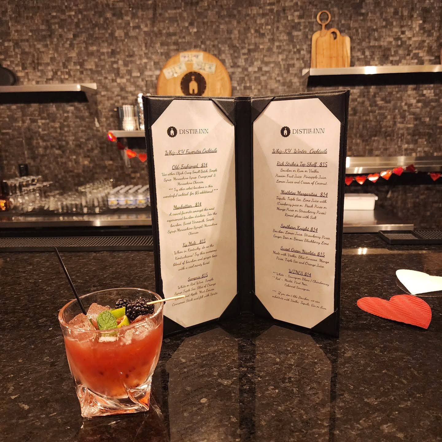 Cocktail on a bar counter beside two upright menu cards, with glasses and bar shelves in the background