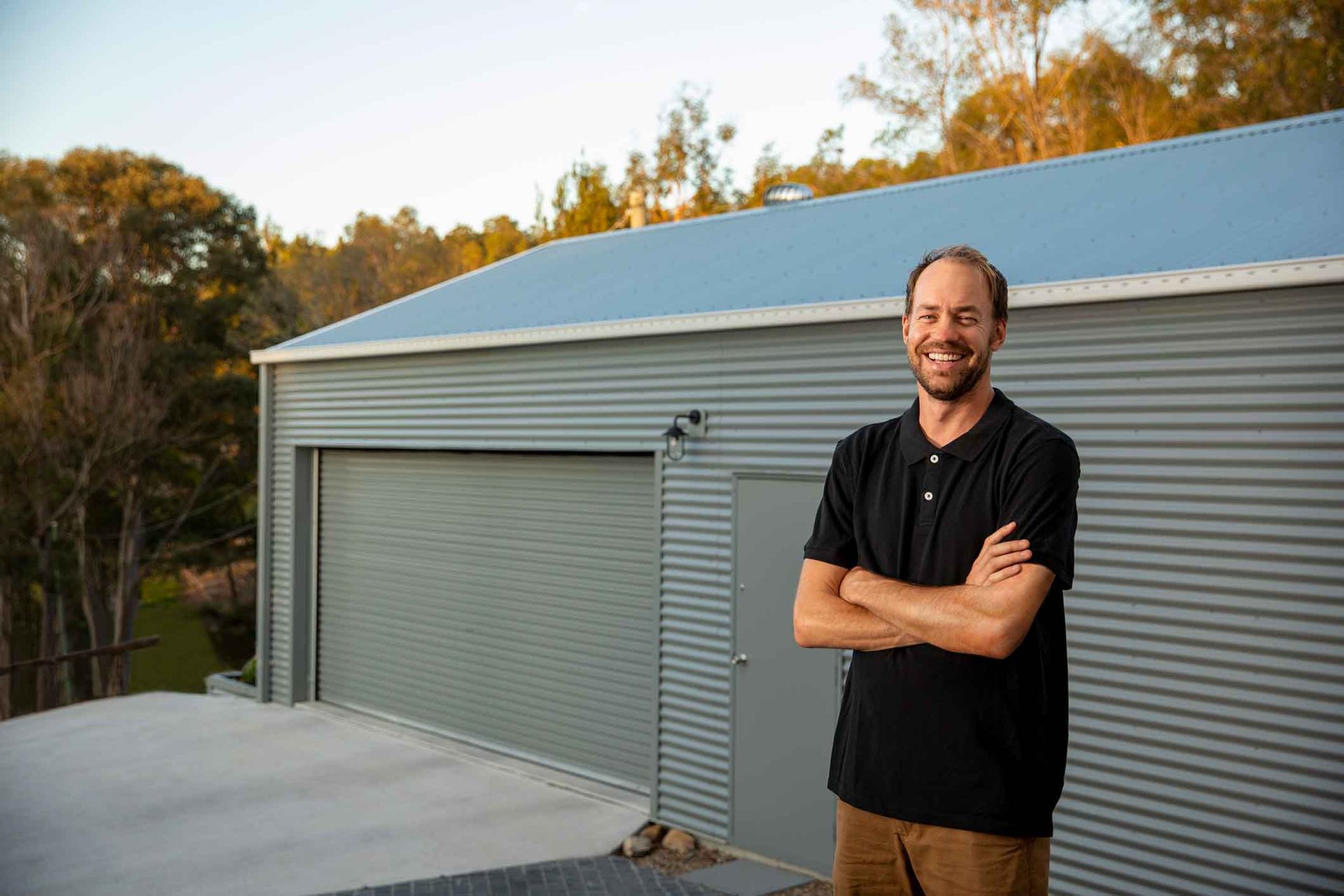 A Man Is Standing In Front Of A Garage With His Arms Crossed – South Kempsey NSW - Fair Dinkum Builds Macleay Valley Sheds