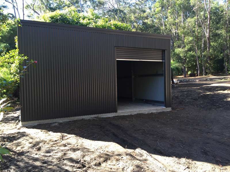 A Black Garage With A Roller Door Is Sitting In The Middle Of A Dirt Field