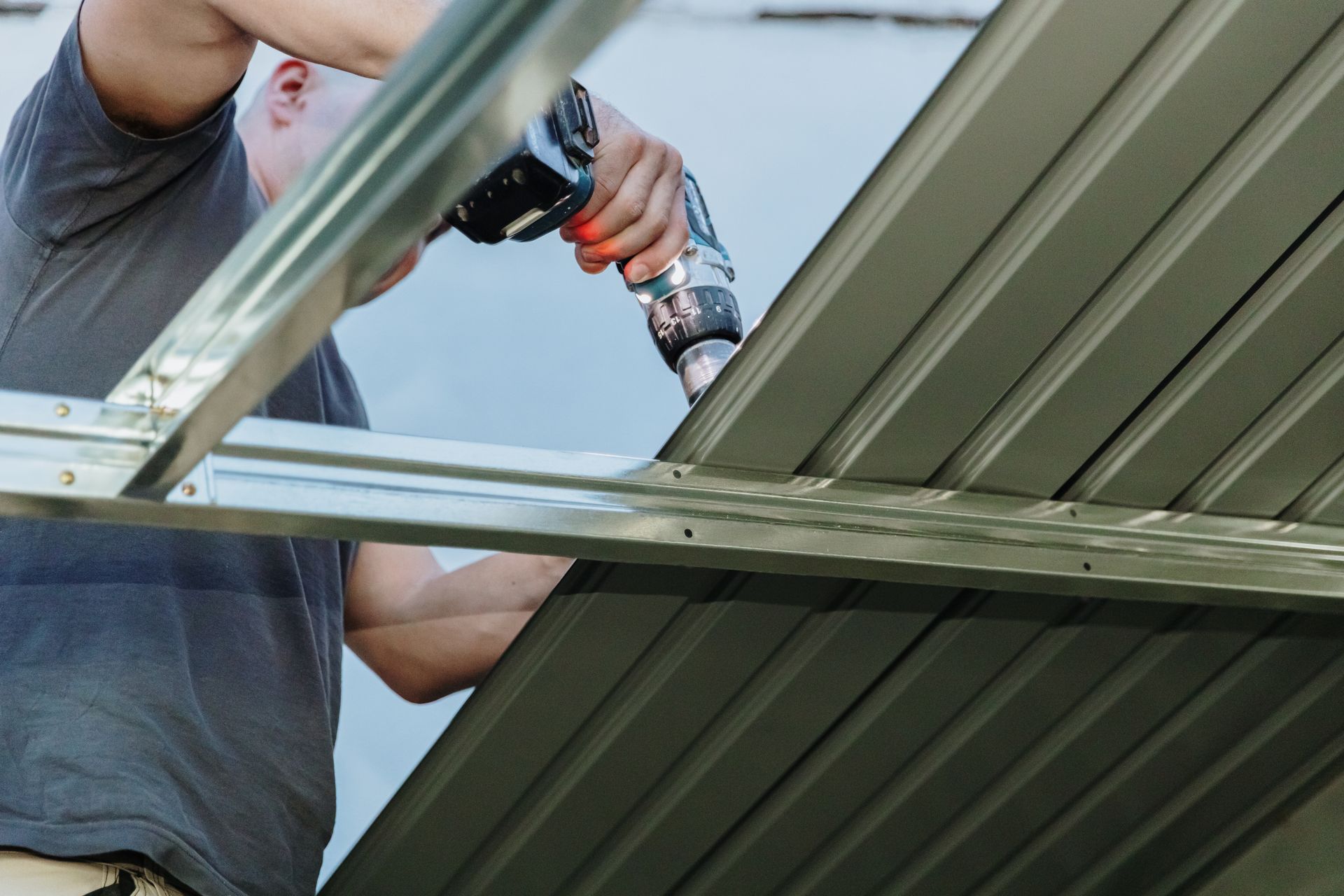 A builder operates a drill while installing a metal shed roof