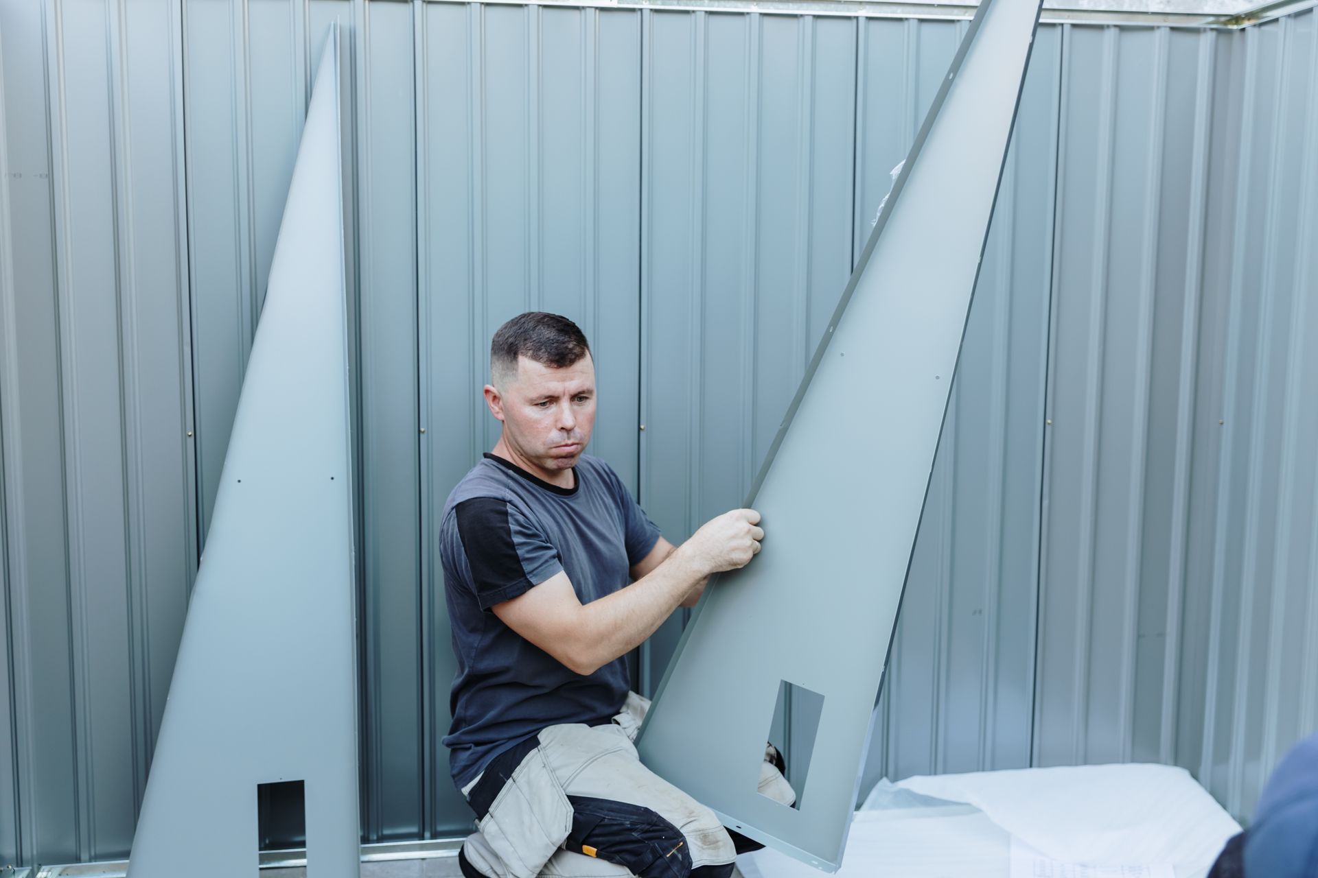 A builder is holding a large metal shed piece, focused on his task
