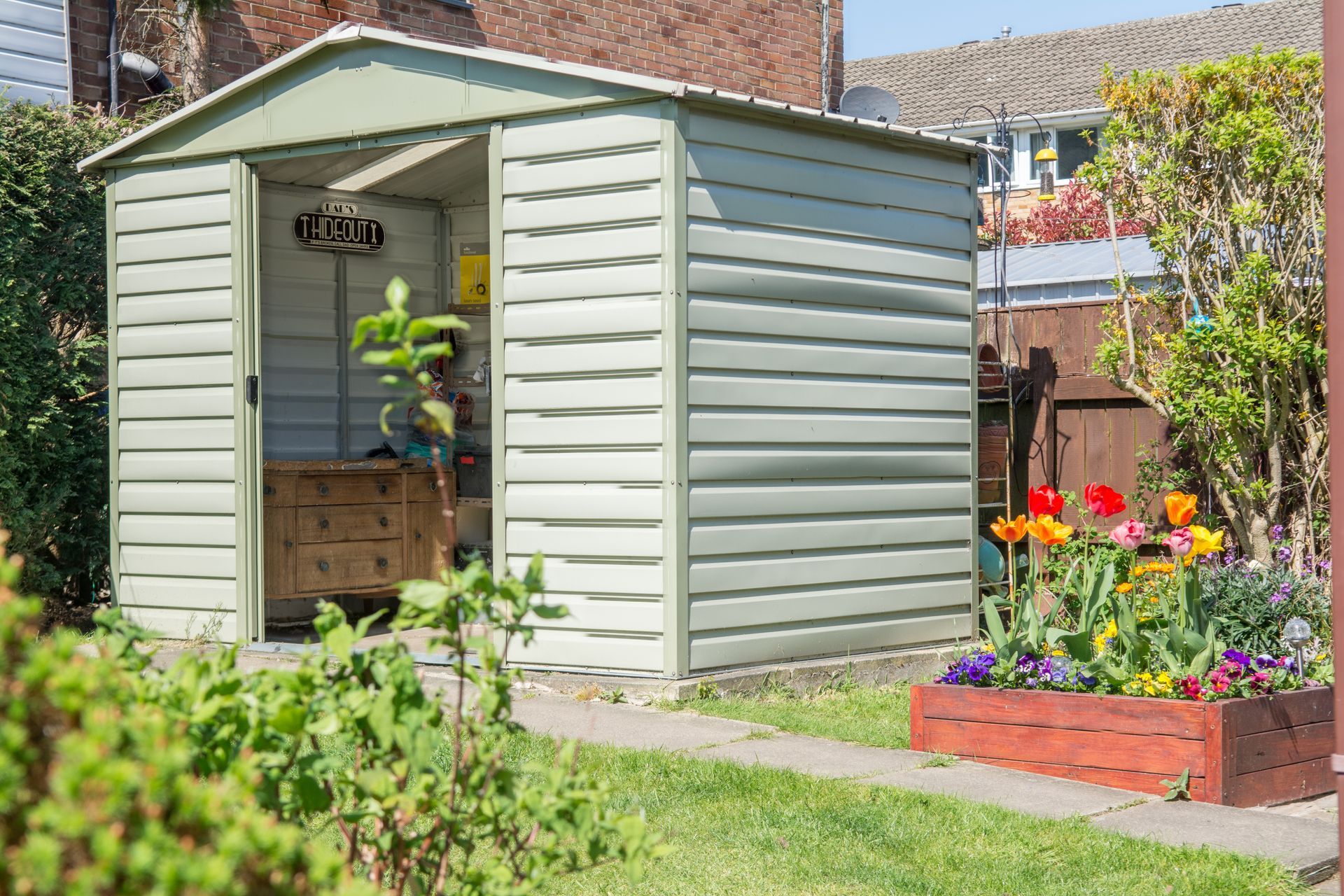 A small shed with a single door, surrounded by grass and a residential garden