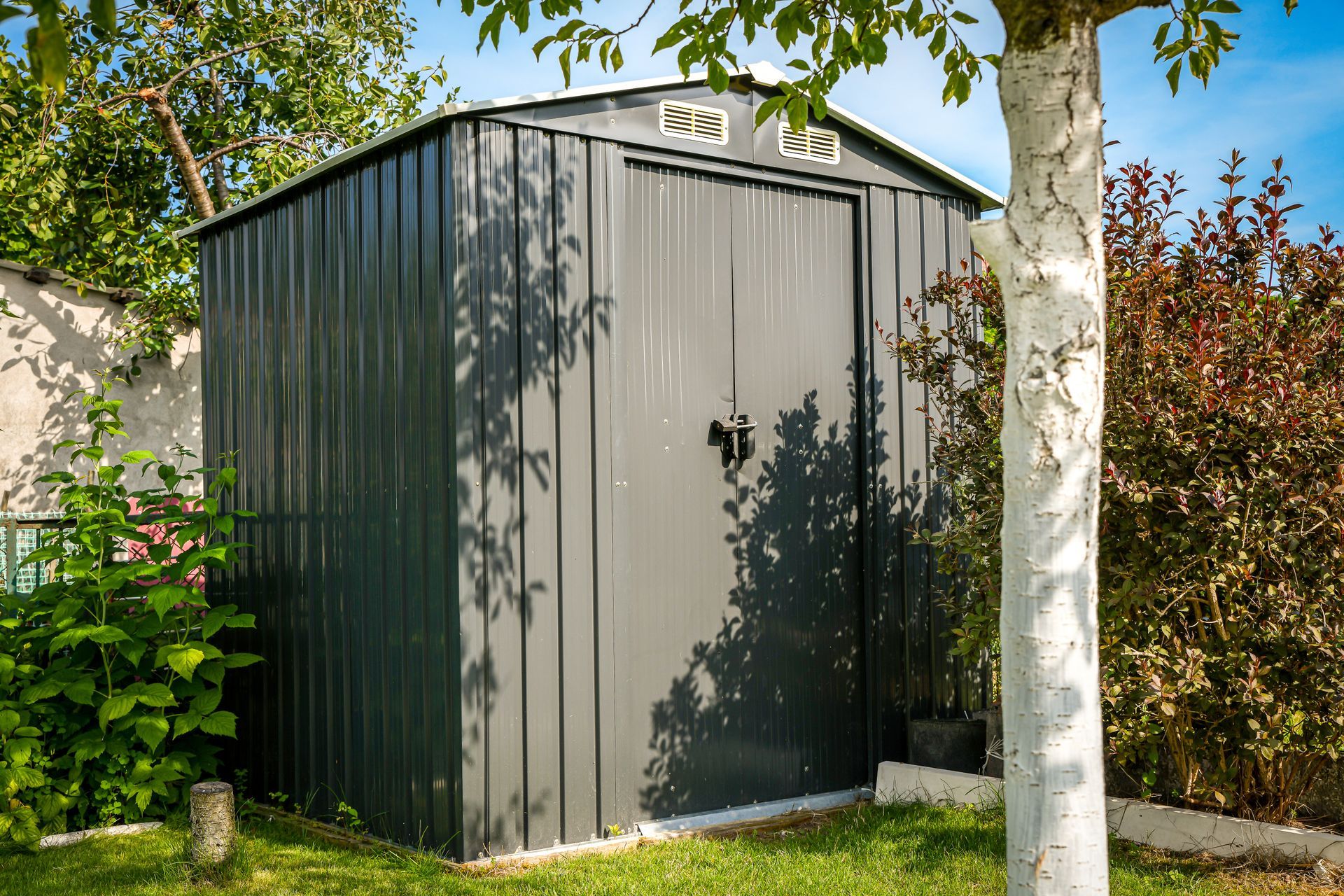 A small black shed situated in a grassy yard, surrounded by trees and shrubs