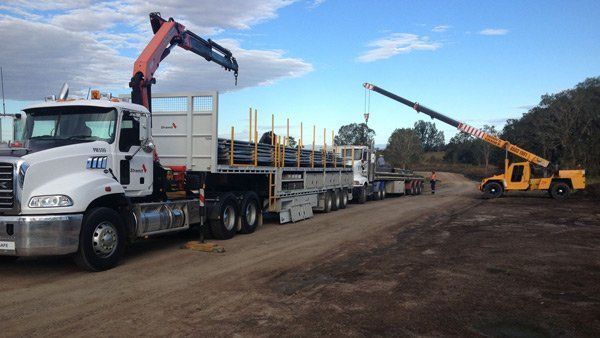 A Truck With A Crane Attached To It Is Driving Down A Dirt Road – South Kempsey NSW - Fair Dinkum Builds Macleay Valley Sheds